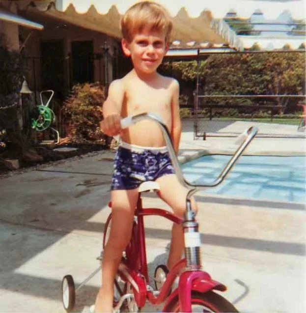 Aboard my first two-wheeler bike (with training wheels) on the patio outside my parents' bedroom, 15472 Huston - 1969